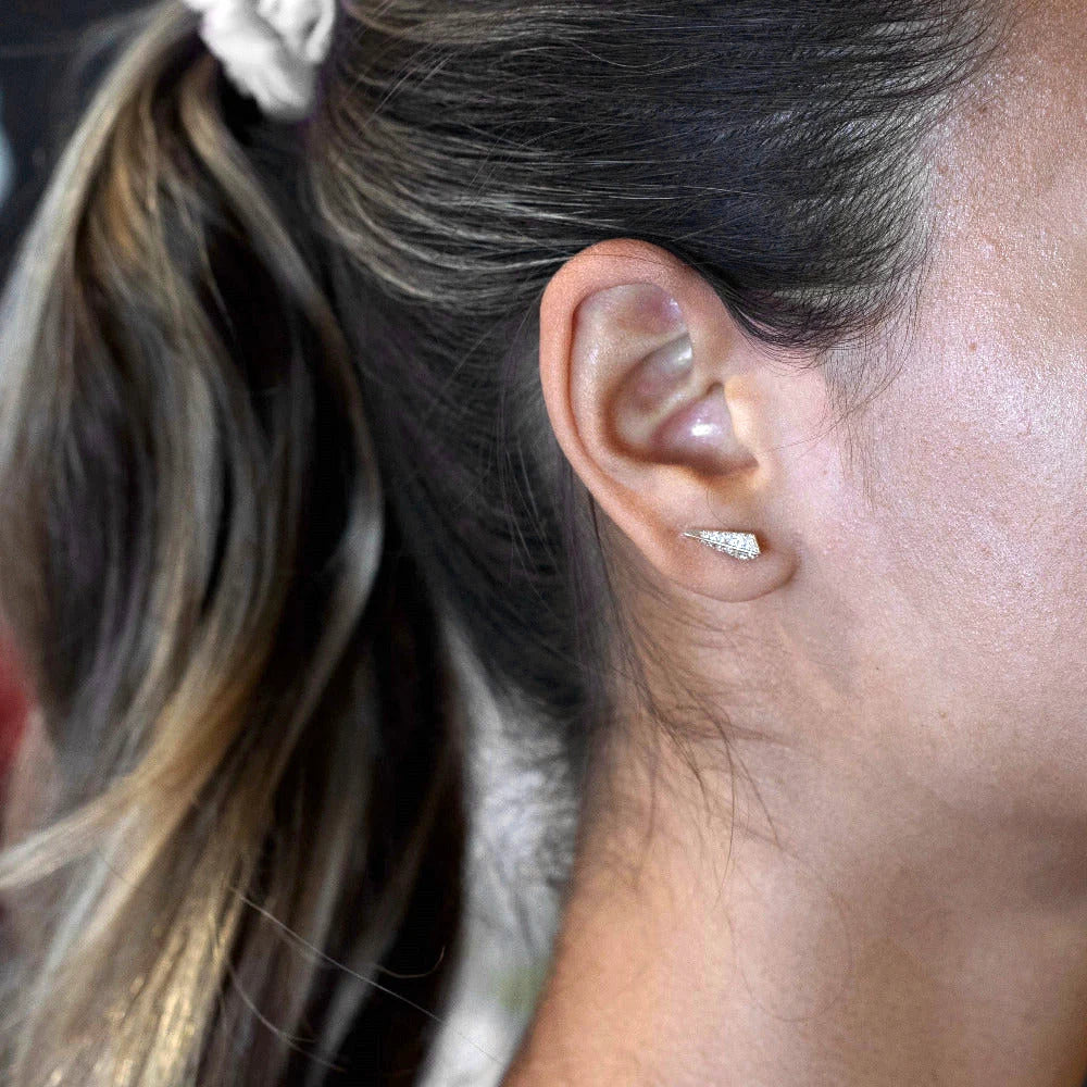 Close-up view of a young woman's ear, featuring a modern, geometric gold earring with diamond pavé. The earring is about the width of the lobe, and is a delicate yet predominantly brilliant piece of jewelry. These studs were designed by Canadian designer Bena Jewelry.