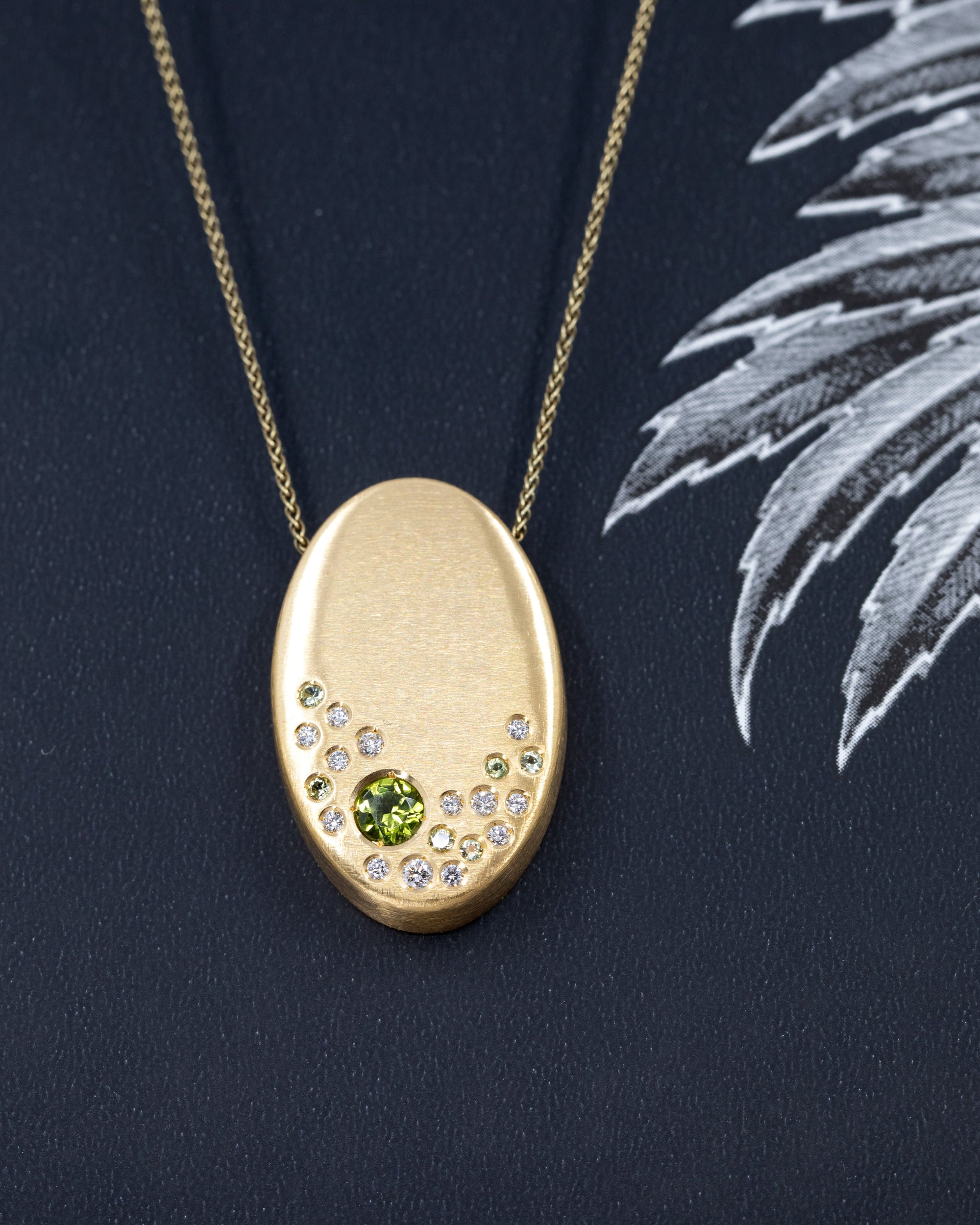 Close-up of the handcrafted gold pendant by Bena Jewelry – Featuring a soft brushed finish, this unique design highlights vibrant green peridots and sparkling diamonds.