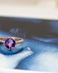 front view of cushion amethyst gemstone rose gold ring custom made in montreal by the bespoke jewellery designer bena jewelry montreal on a blue background
