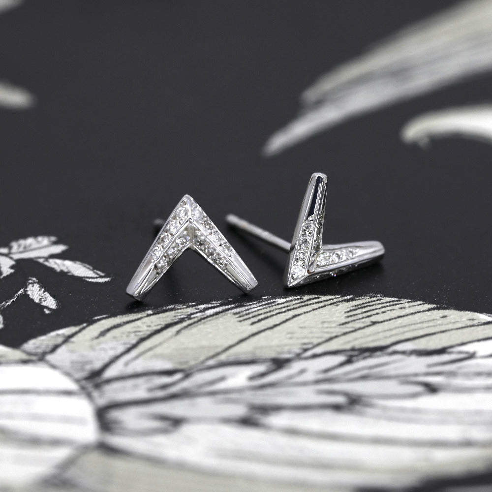 The Arrow Diamond Studs displayed on a slate-gray background, emphasizing the contrast between the white gold and the brilliance of the diamonds.