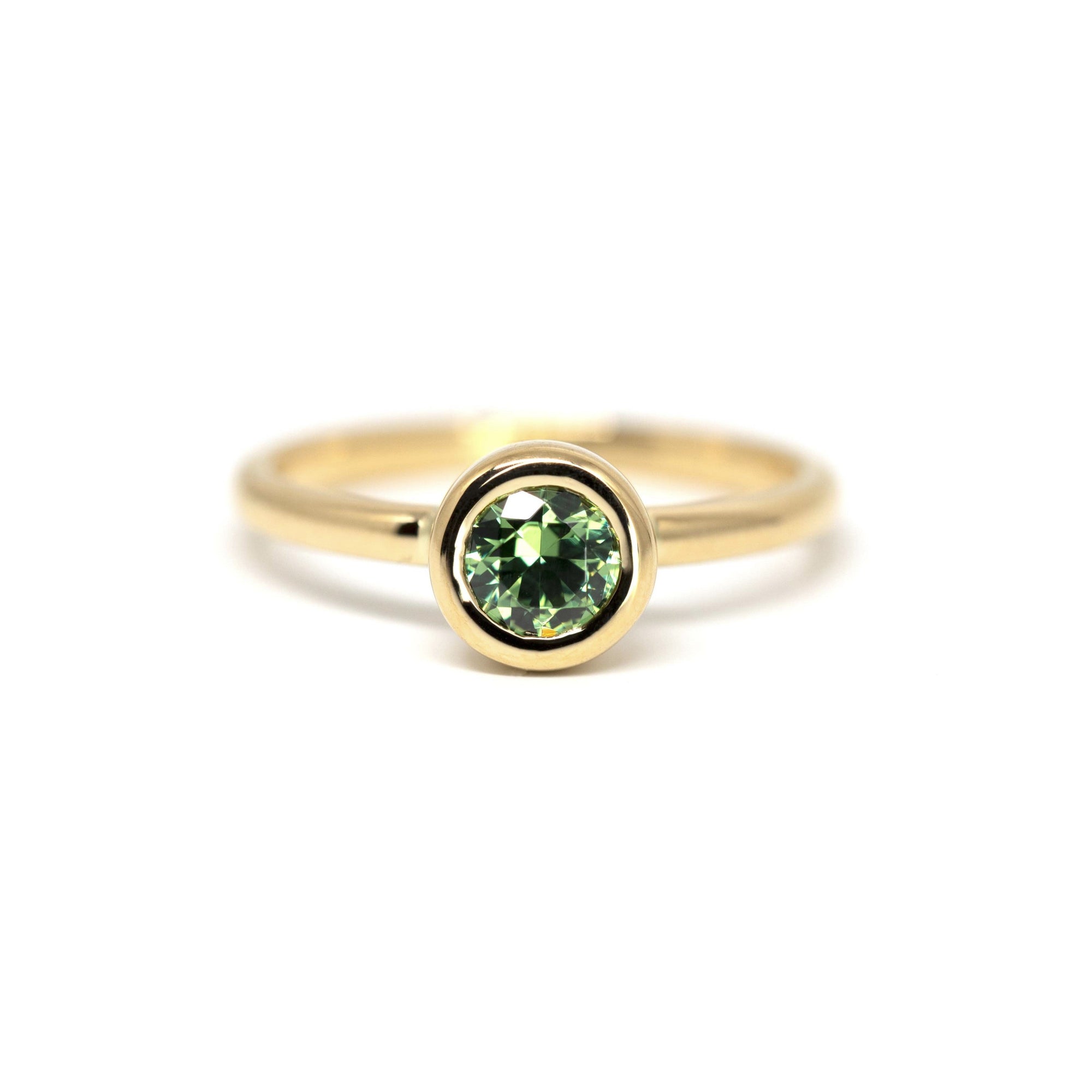 Bezel Set Demantoide Ring by Bena Jewelry, featuring a vibrant green demantoid garnet in a round cut, set in yellow gold. Photographed on a white background.