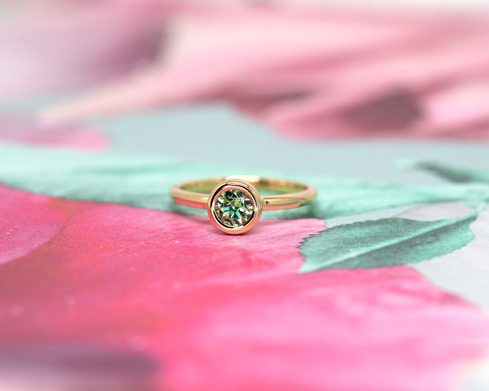Elegant Bezel Set Demantoide Ring in yellow gold, featuring a natural green garnet, showcased on a soft pink and floral background. Made in Canada.