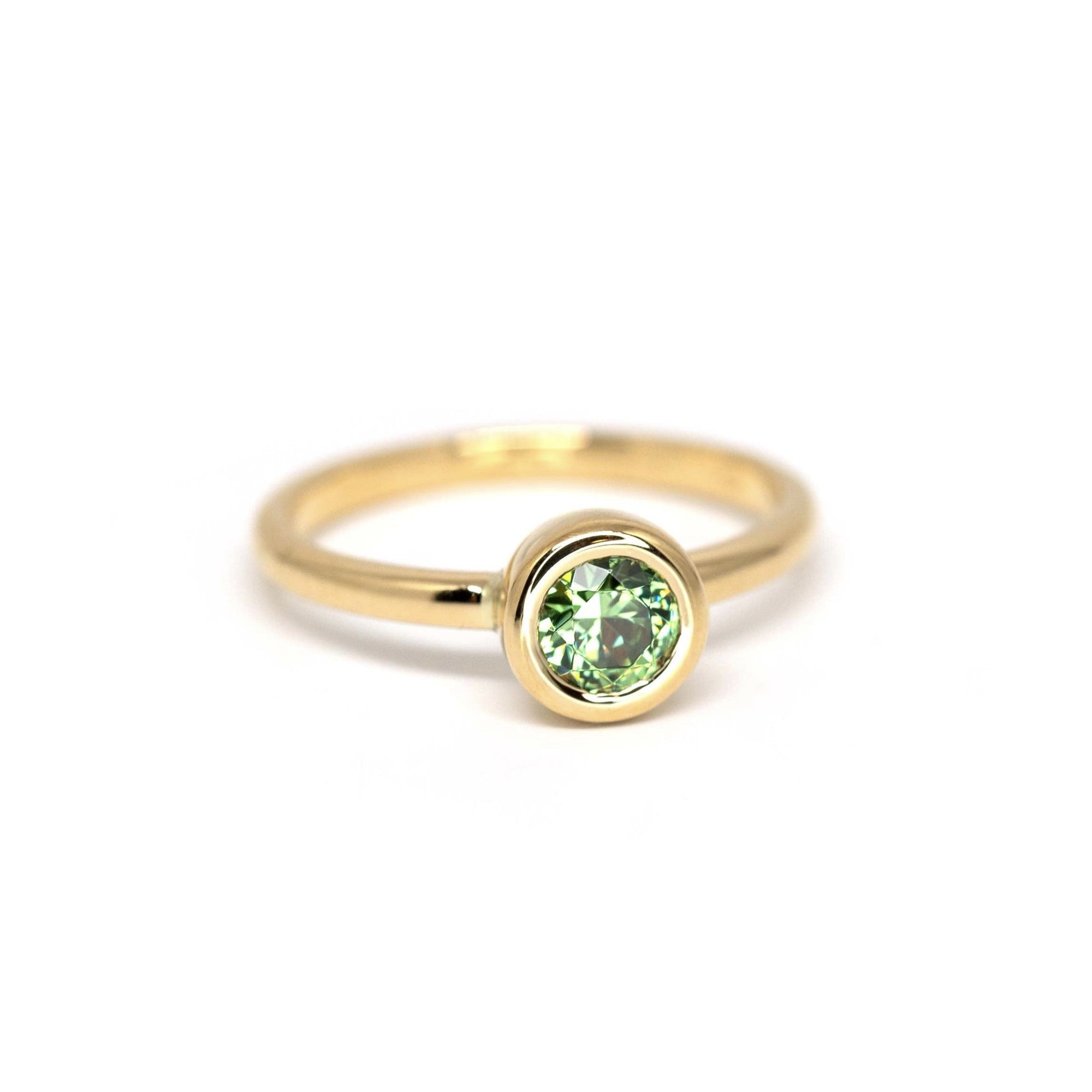 Elegant yellow gold ring featuring a green demantoid garnet by Bena Jewelry, photographed on a plain white background. Minimalist design, made in Montreal.