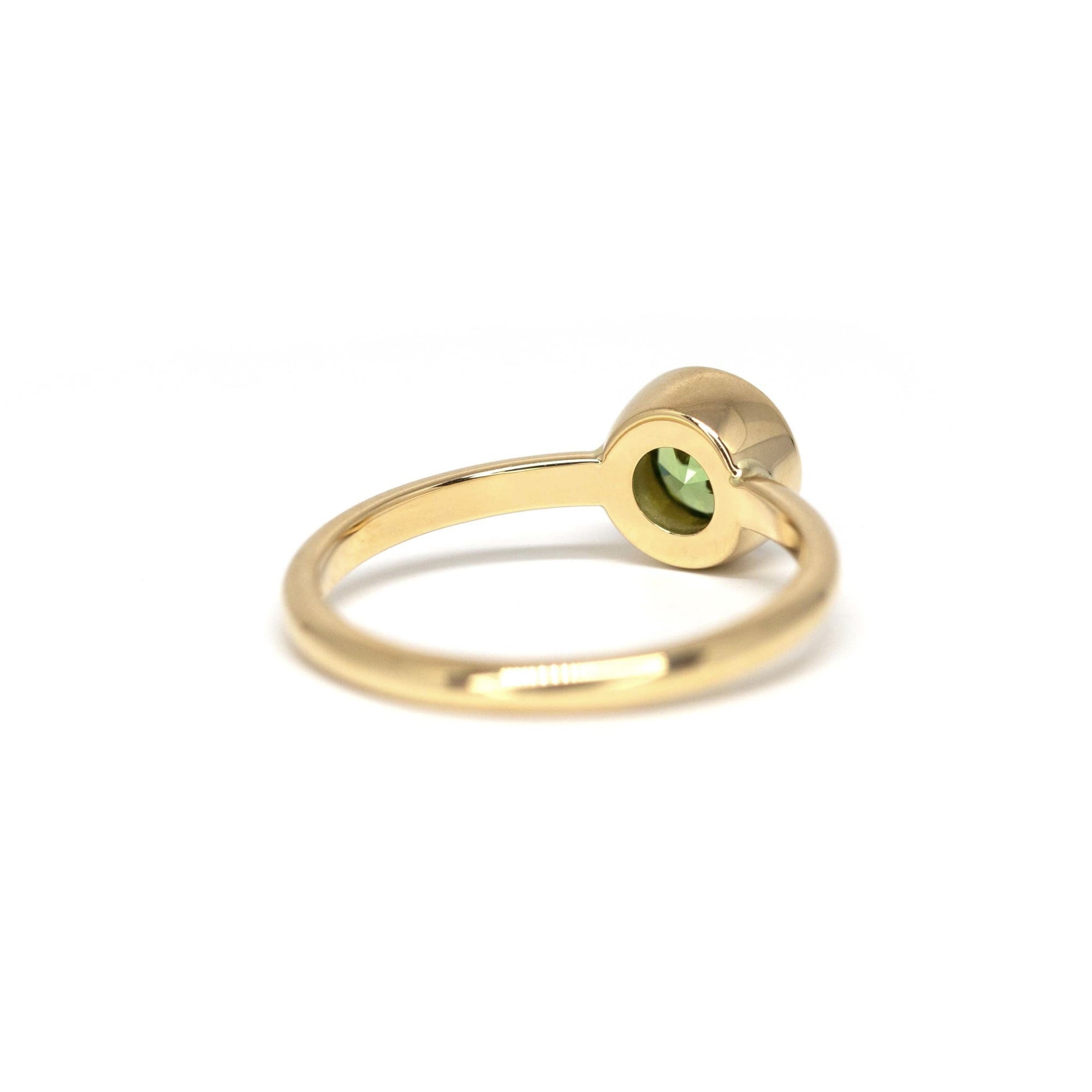Bezel Set Demantoide Ring in yellow gold, showcasing a round-cut green garnet, crafted by Bena Jewelry. Photographed on a white background, custom-made in Montreal.