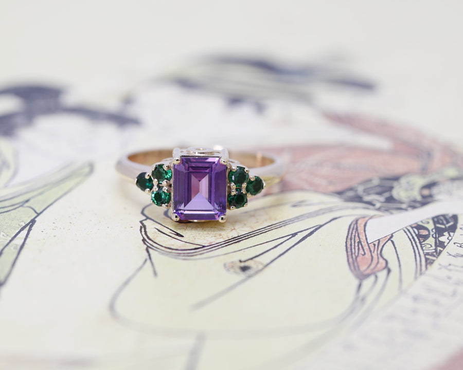 front view of amethyst statement ring and small round emerald gemstone custom made in montreal by the best designer bena jewelry on multi color background