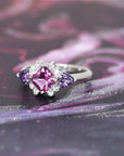 side view of purple pink sapphire square shape and trillon diamond platinum ring custom made in montreal by bena jewelry designer at ruby mardi on a dark multi color background