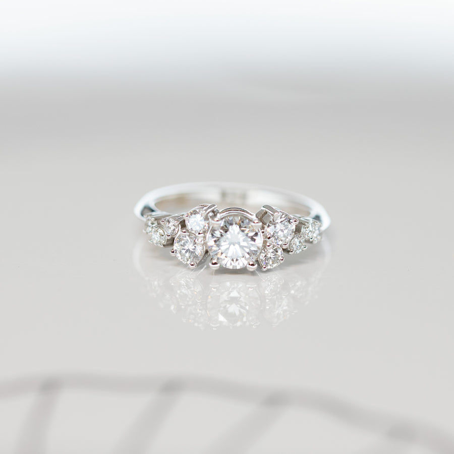 front view of white gold engagement with a round central diamond and many smallers diamonds all over the band made on a grey background