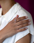Close-up of a woman’s hand wearing the Diamond Halo Pink Sapphire Ring in white gold, showcasing the vibrant pink sapphire and delicate diamond halo, handcrafted by Bena Jewelry.