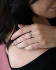 White gold engagement ring featuring an oval pink sapphire surrounded by diamonds, Diamond Halo Pink Sapphire Ring by Bena Jewelry, shown in a close-up on a woman’s hand.