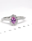 Diamond Halo Pink Sapphire Ring in white gold featuring an oval pink sapphire surrounded by diamonds, photographed on a white background, custom bridal jewelry by Bena Jewelry.