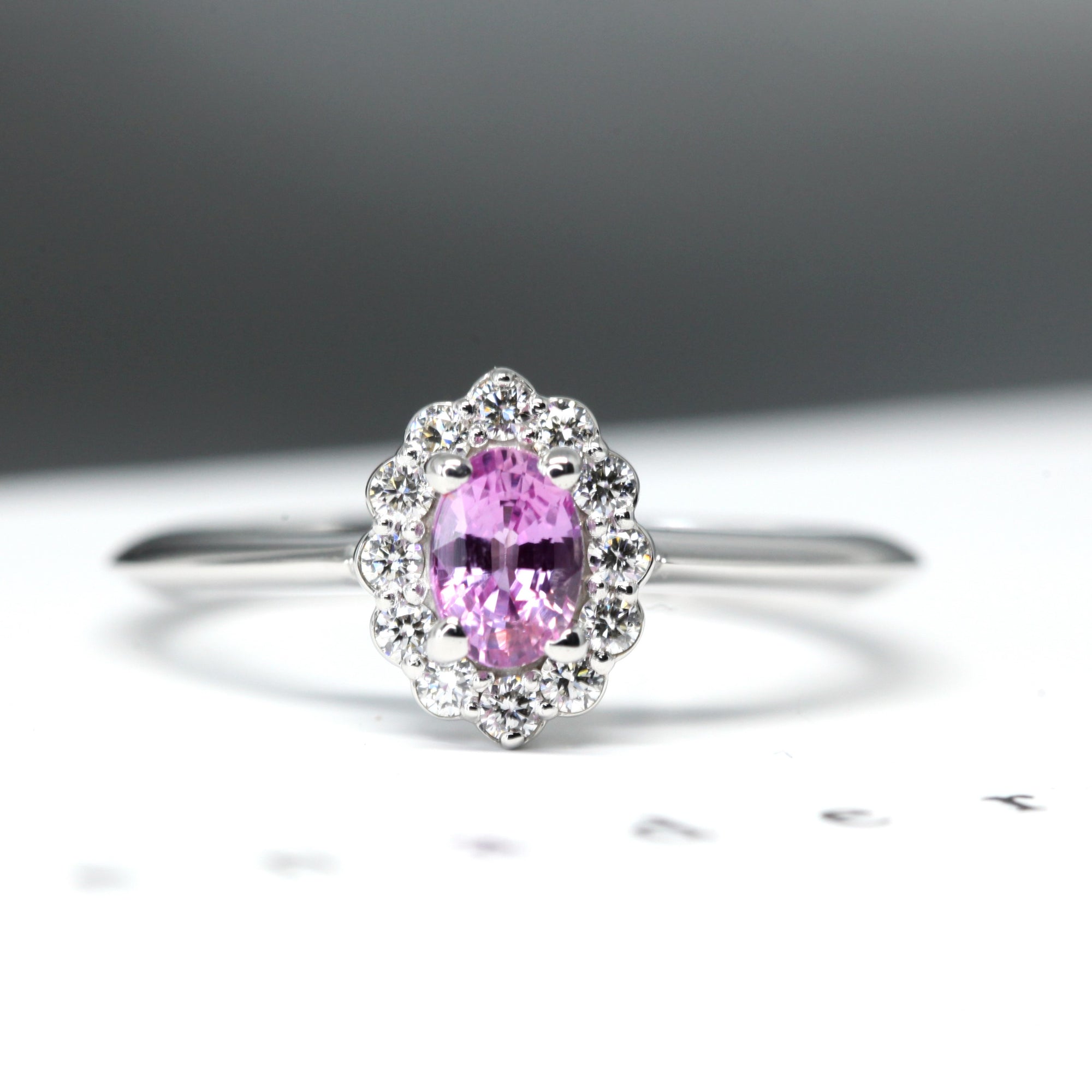 Front view of white gold bridal ring with a diamond halo and pink sapphire, Diamond Halo Ring by Bena Jewelry, displayed on a white background, handmade in Montreal.