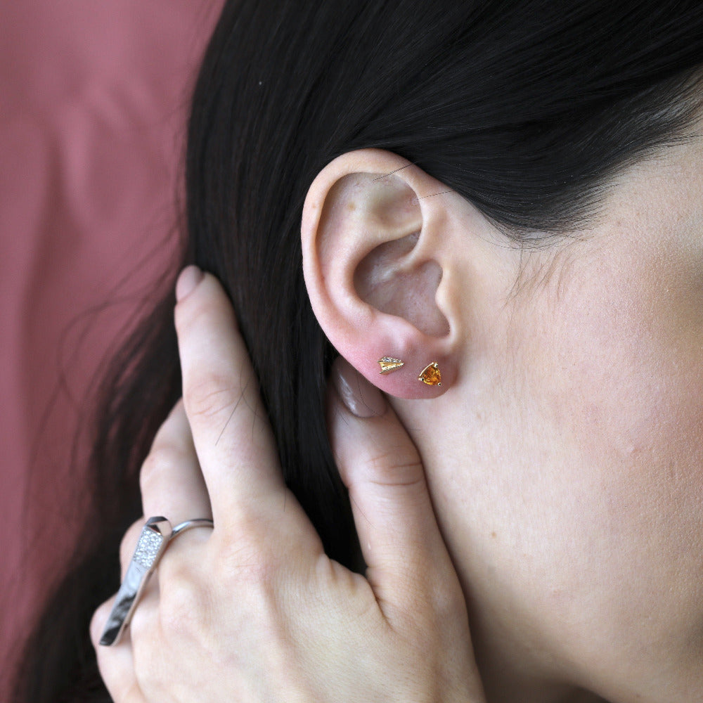 Girl wearings orange sapphire gemstone stud earrings and small minimalist yellow gold diamond stud earrings and double finger ring by Bena Jewelry Montreal.