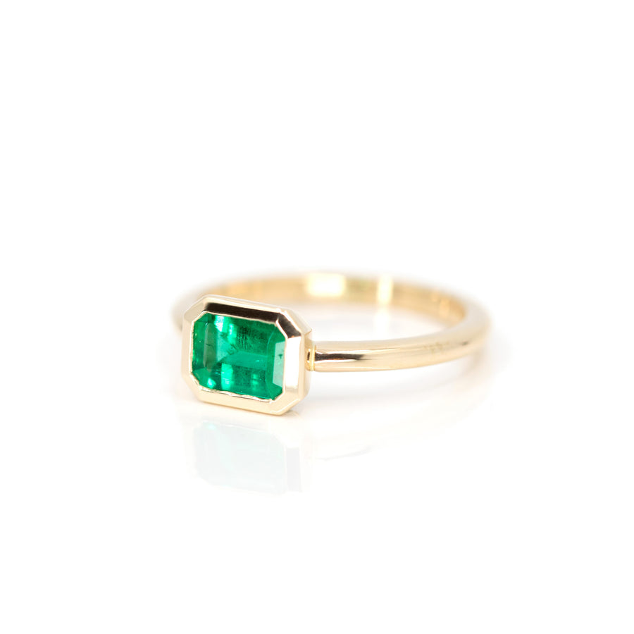 side view of designer bridal engagement ring cusotm made in montreal yellow gold bezel setting emerald ring on white background