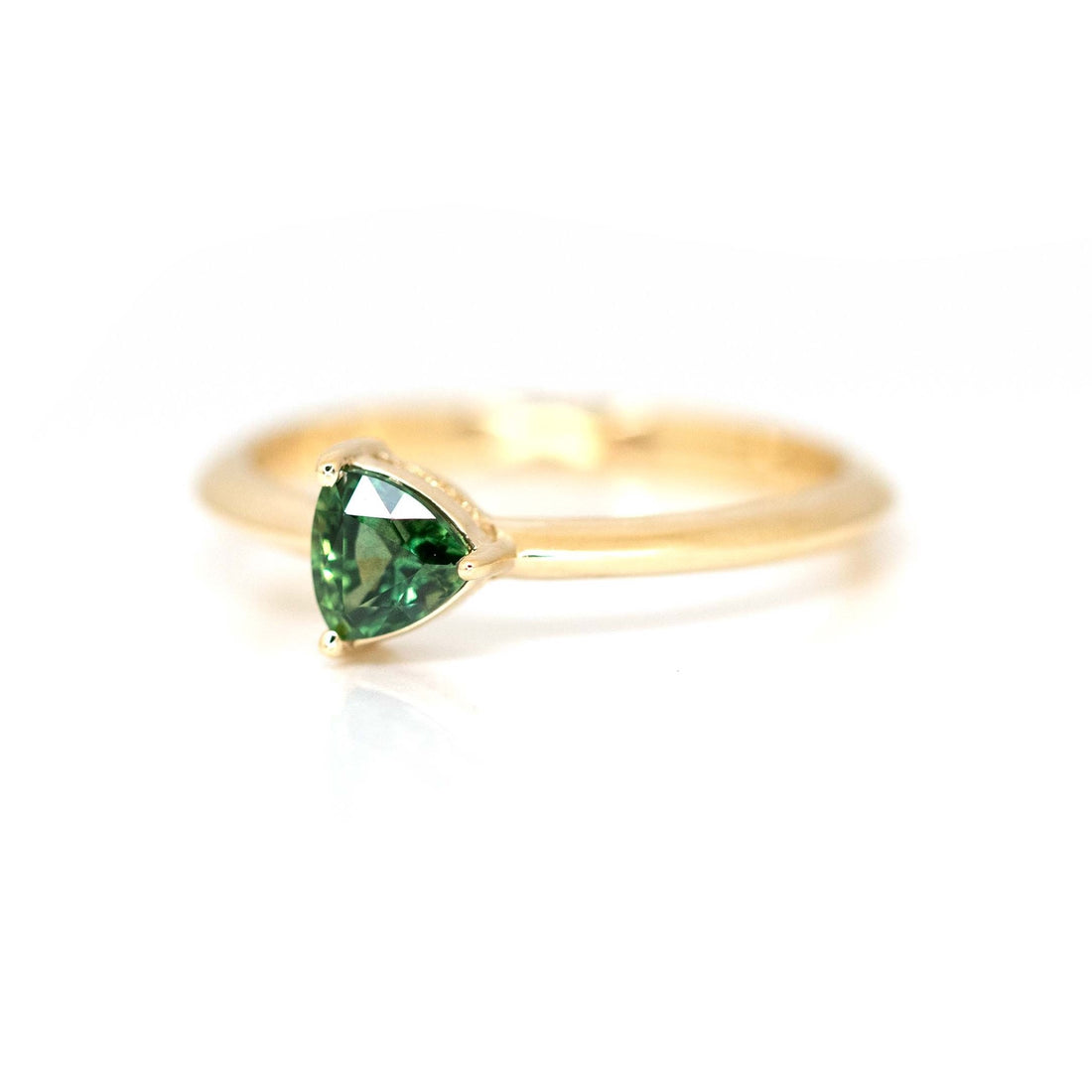 side view of green sapphire yellow gold ring on a white background