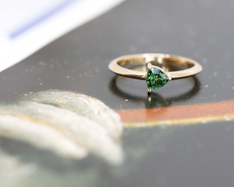 splendid ring with a trillion shaped green gemstone custom made in Montreal on a black background