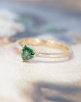 side view of the ring with a trillion-shaped green sapphire mounted on a yellow gold engagement ring made in Montreal on a multicolored background