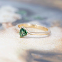 side view of the ring with a trillion-shaped green sapphire mounted on a yellow gold engagement ring made in Montreal on a multicolored background