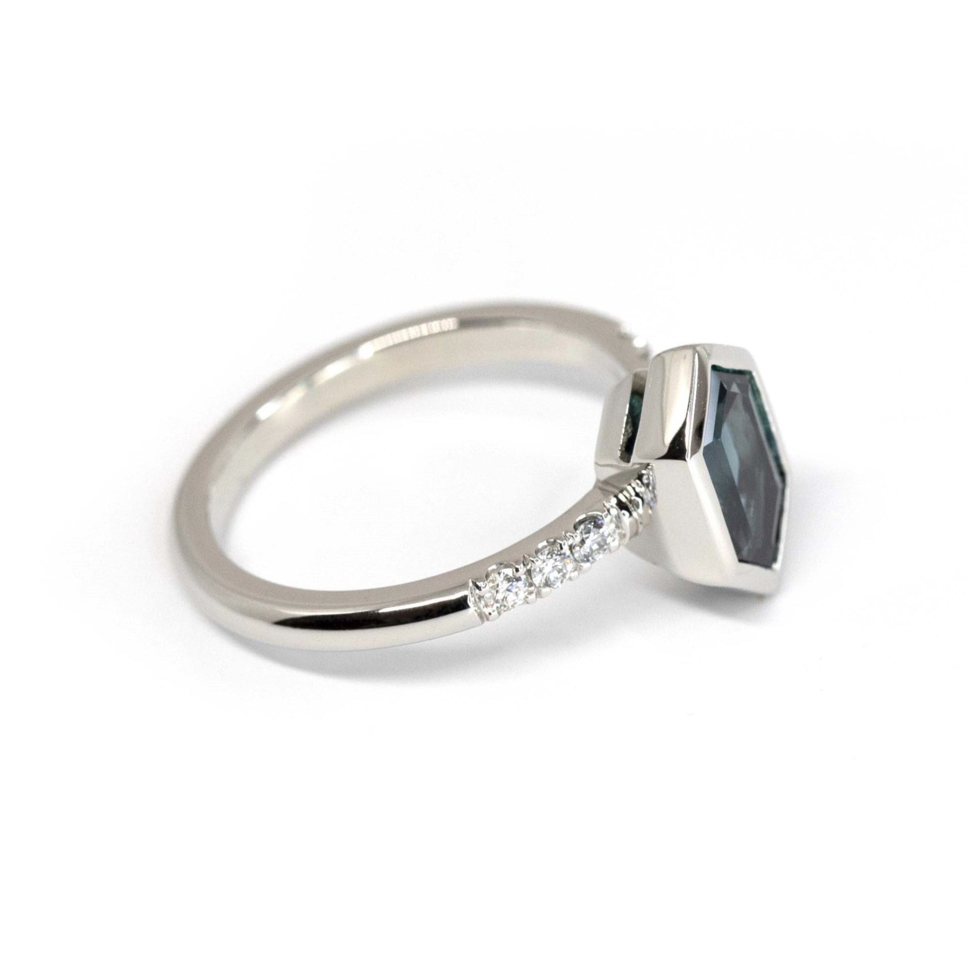 Close-up of blue sapphire ring – A custom-made engagement ring with a striking electric blue hexagonal sapphire, bezel-set in platinum, flanked by diamonds.