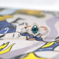 front view of custom made montana blue green sapphire diamond halo rose gold ring made in montreal on multi color background