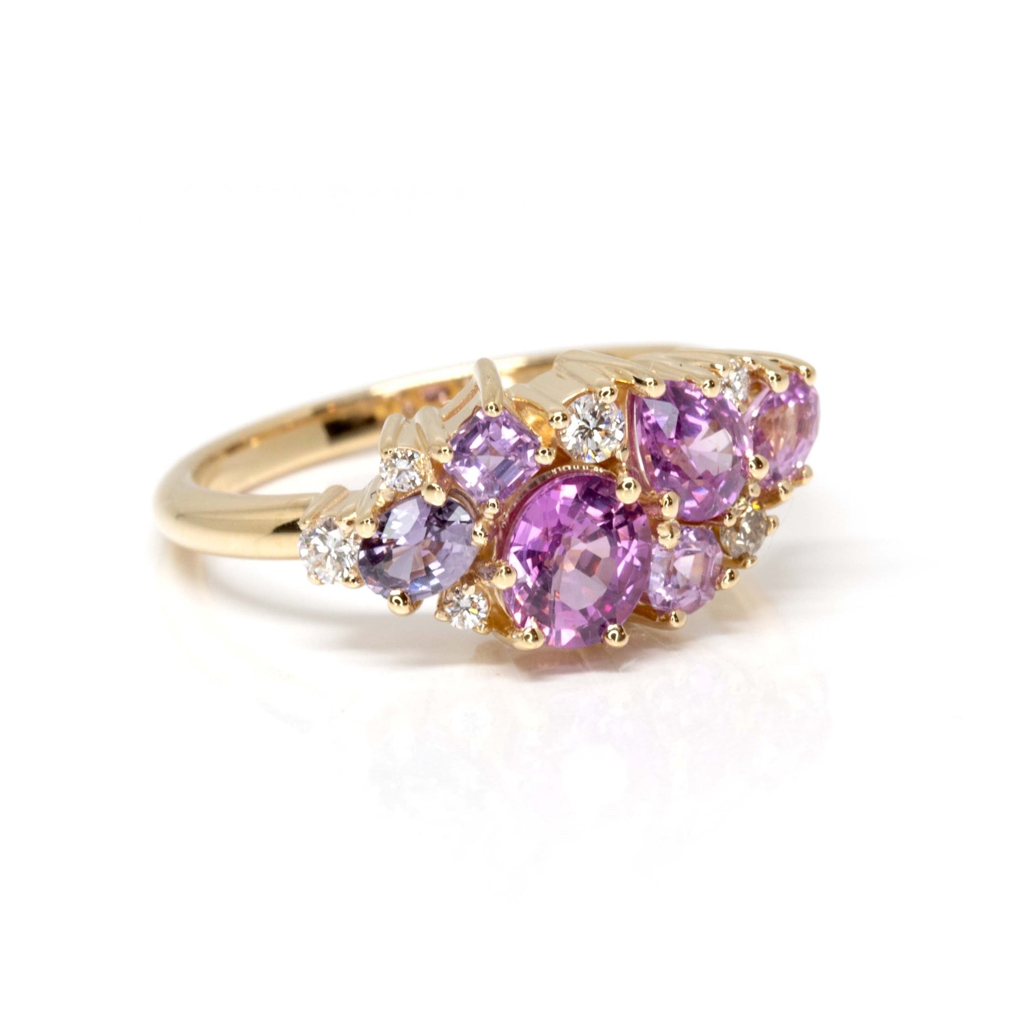 The Avalanche Pink Sapphire Ring against a dark background, emphasizing the vibrant sapphires and diamonds in the warm yellow gold setting. Designed by Bena Jewelry, Montreal, Canada.