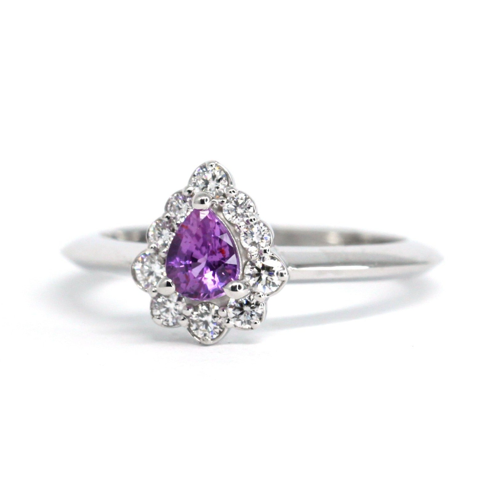 Sleek white gold band supporting a pear-cut pink-violet sapphire, complemented by a radiant halo of diamonds. Handmade in Montreal by independent jewelry designer Bena Jewelry.