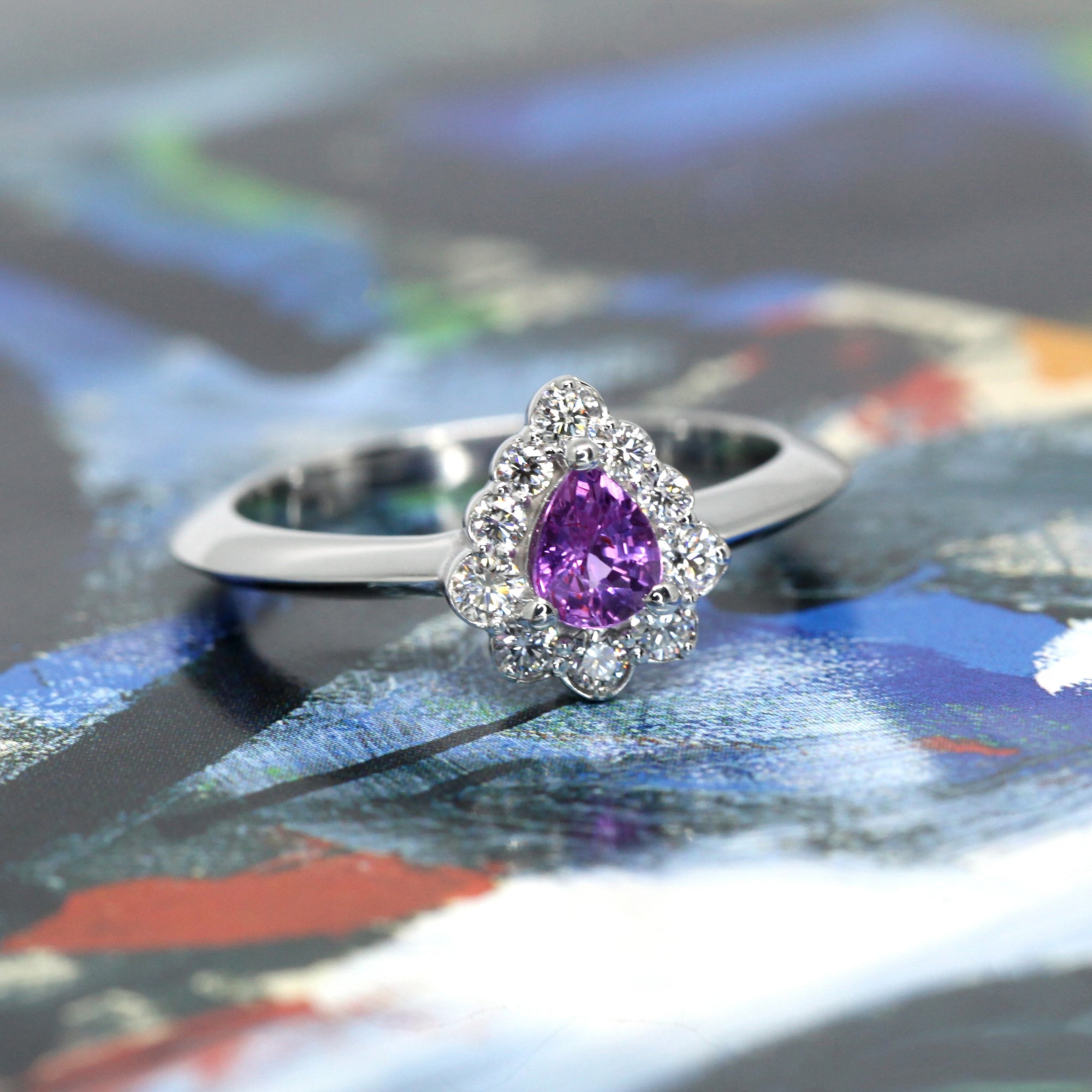 A luxurious engagement ring with a pear-shaped sapphire and diamonds, set in white gold and showcased on a colorful background.