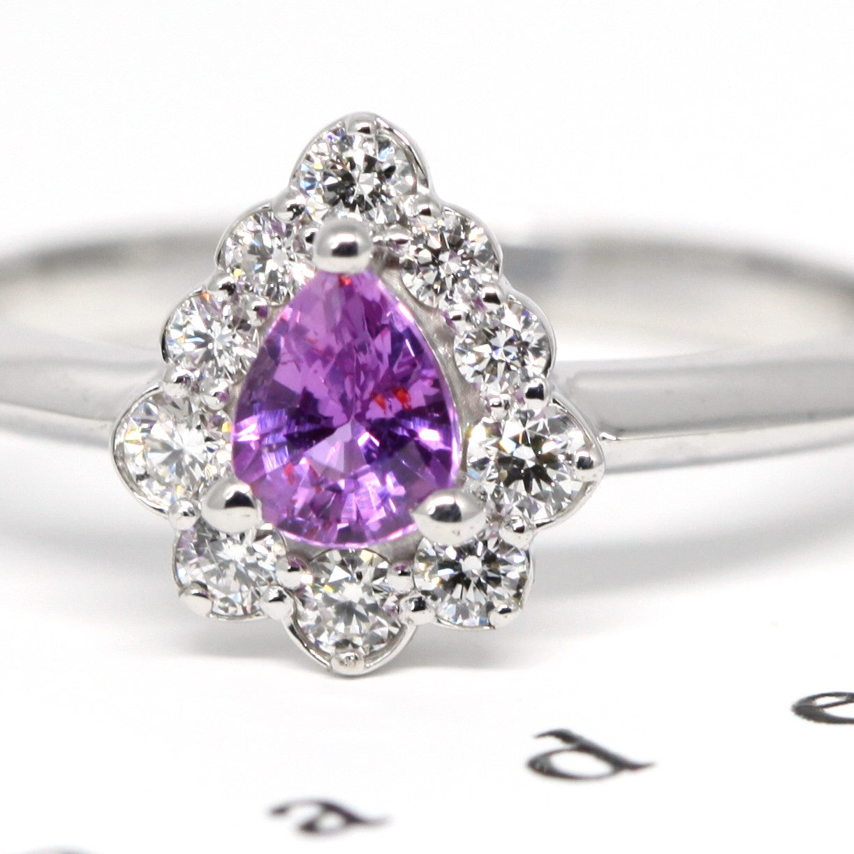 Delicate engagement ring with a pear-cut sapphire and diamond halo, emphasizing the brilliance of its custom-made design. Designed and crafted by Bena Jewelry in Montreal, Canada.