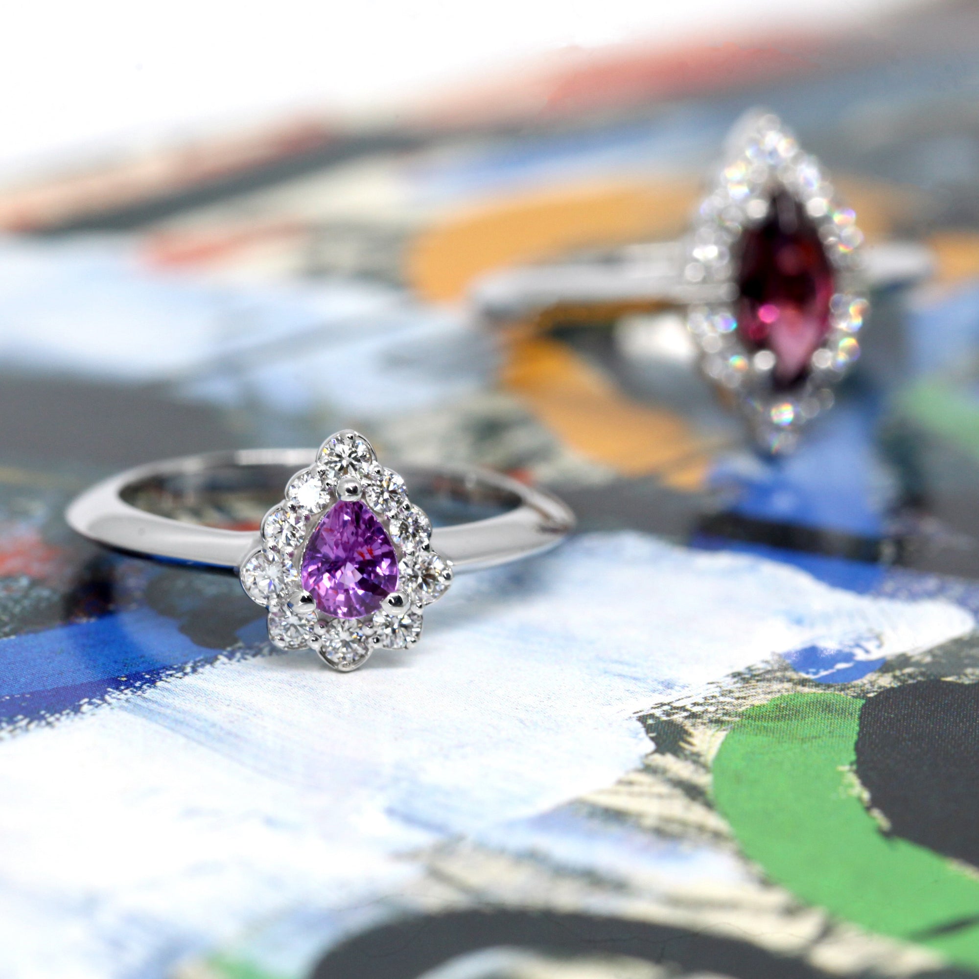 The Aura ring displayed against a soft-hued backdrop, enhancing the vibrancy of its pink-violet sapphire and diamond halo.