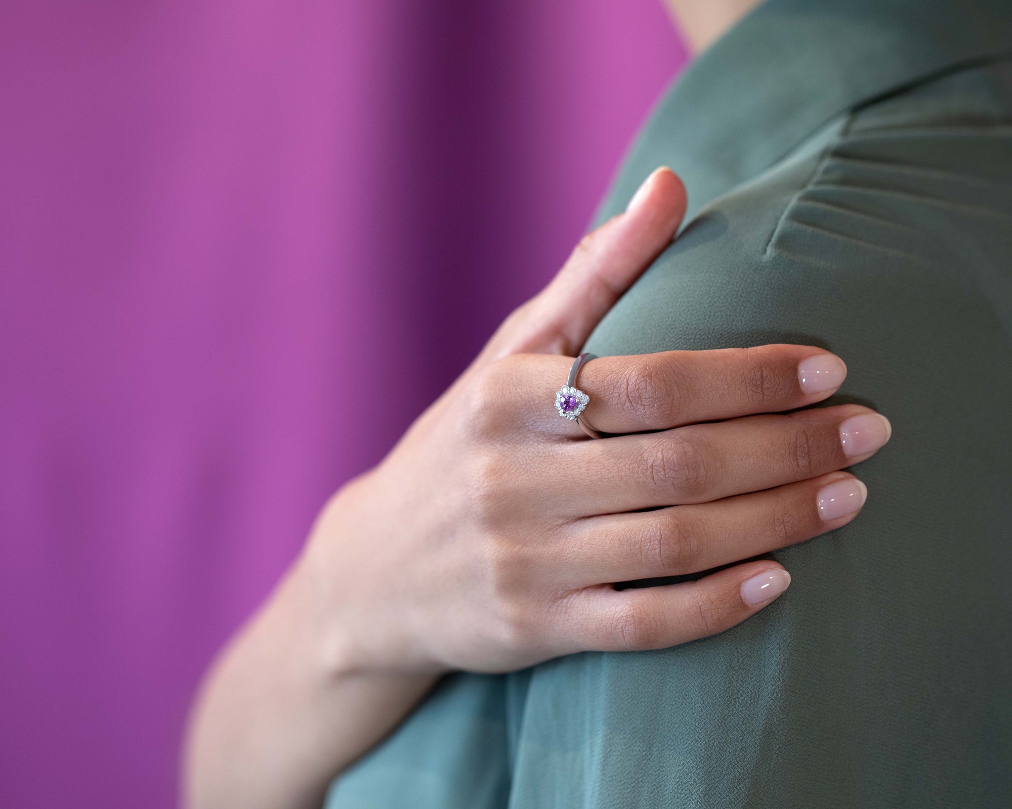 Close-up of the Aura engagement ring on the finger, showcasing the radiant pink-violet sapphire and brilliant diamond halo.