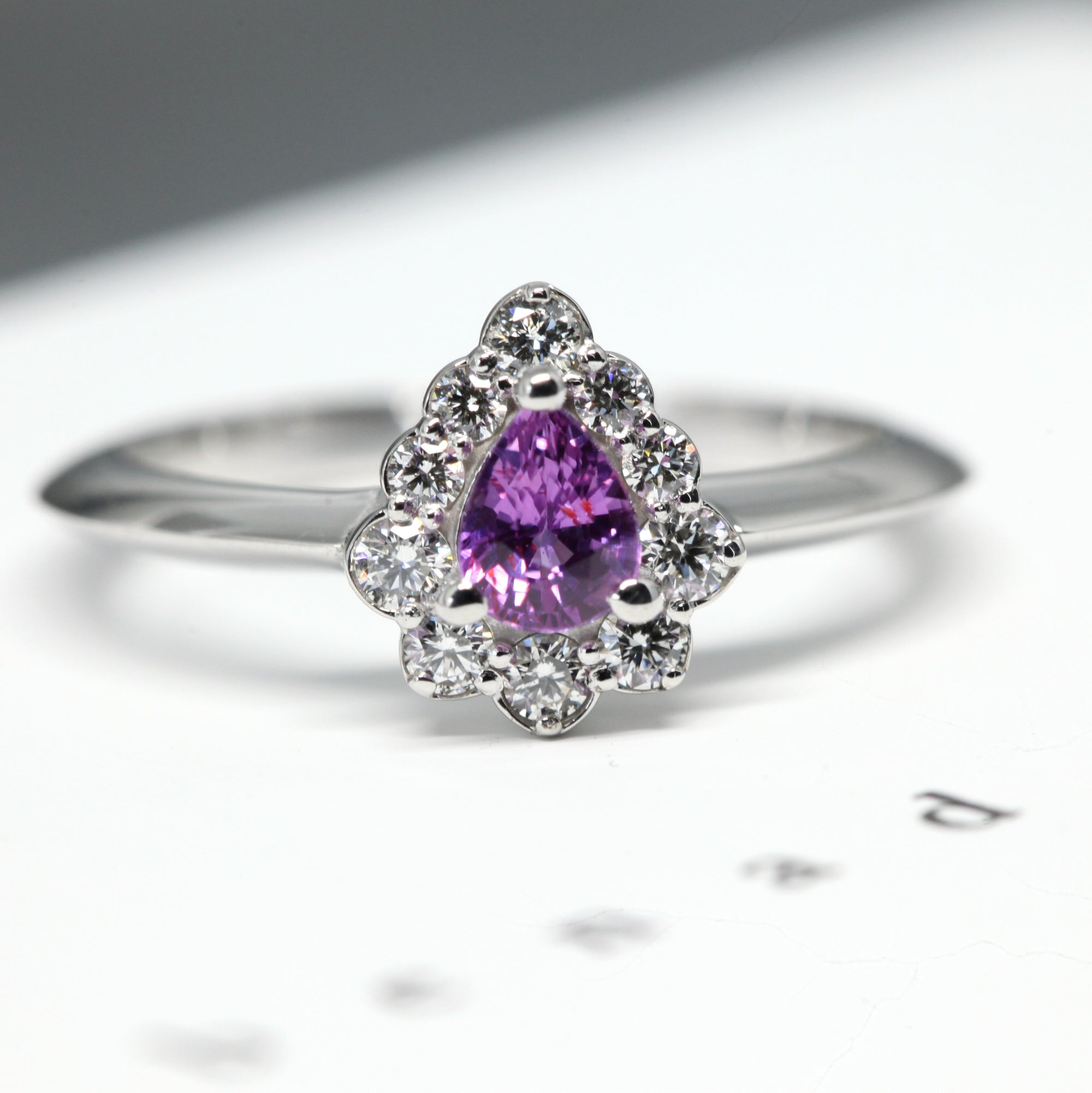 Aura engagement ring featuring a pear-cut pink-violet sapphire with a diamond halo, set in polished white gold. Handmade in Montreal by Bena Jewelry, a Canadian designer.