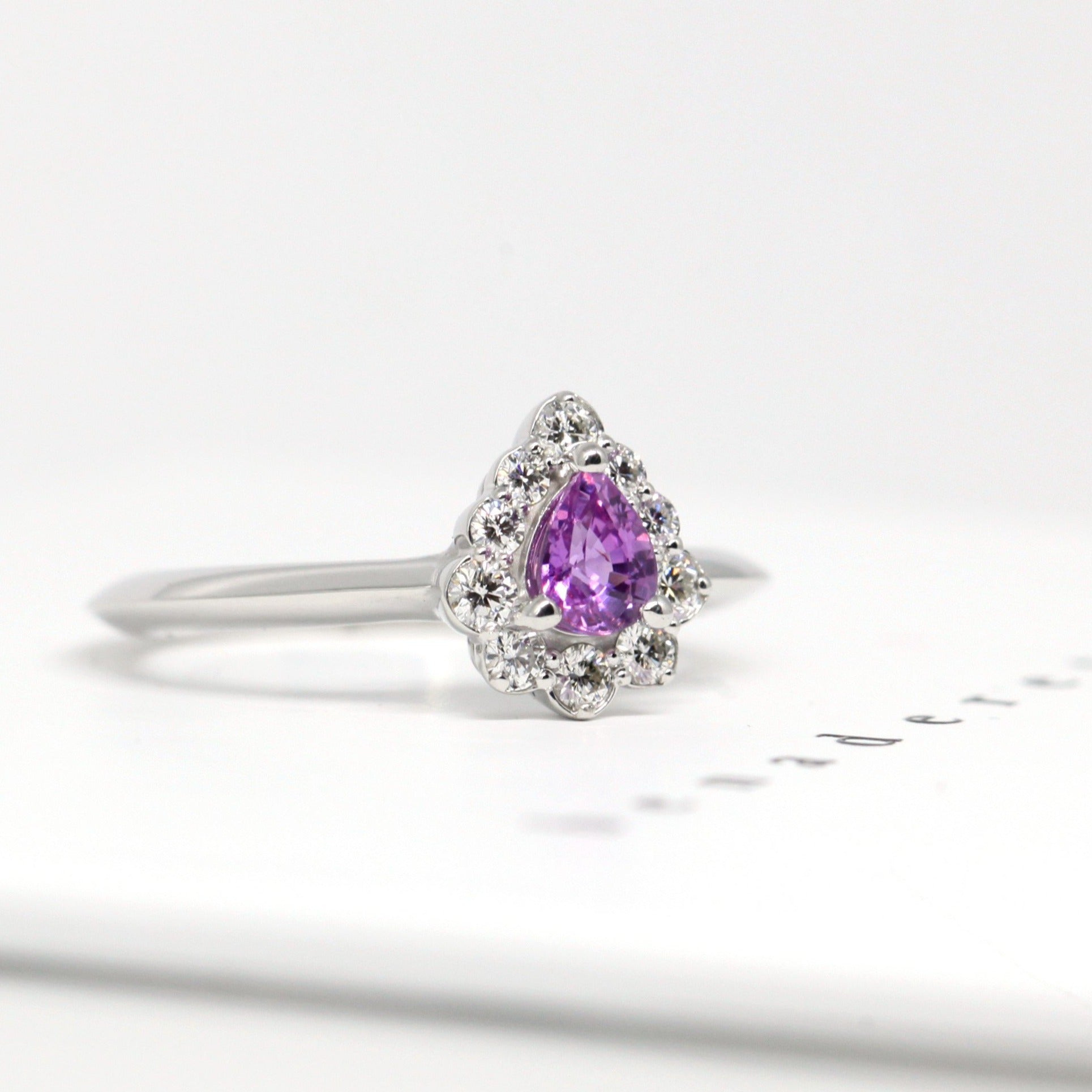 Close-up of the Aura ring, highlighting its pear-shaped pink-violet sapphire and surrounding diamond halo. A timeless engagement piece in white gold, crafted by Bena Jewelry in Montreal, Canada.