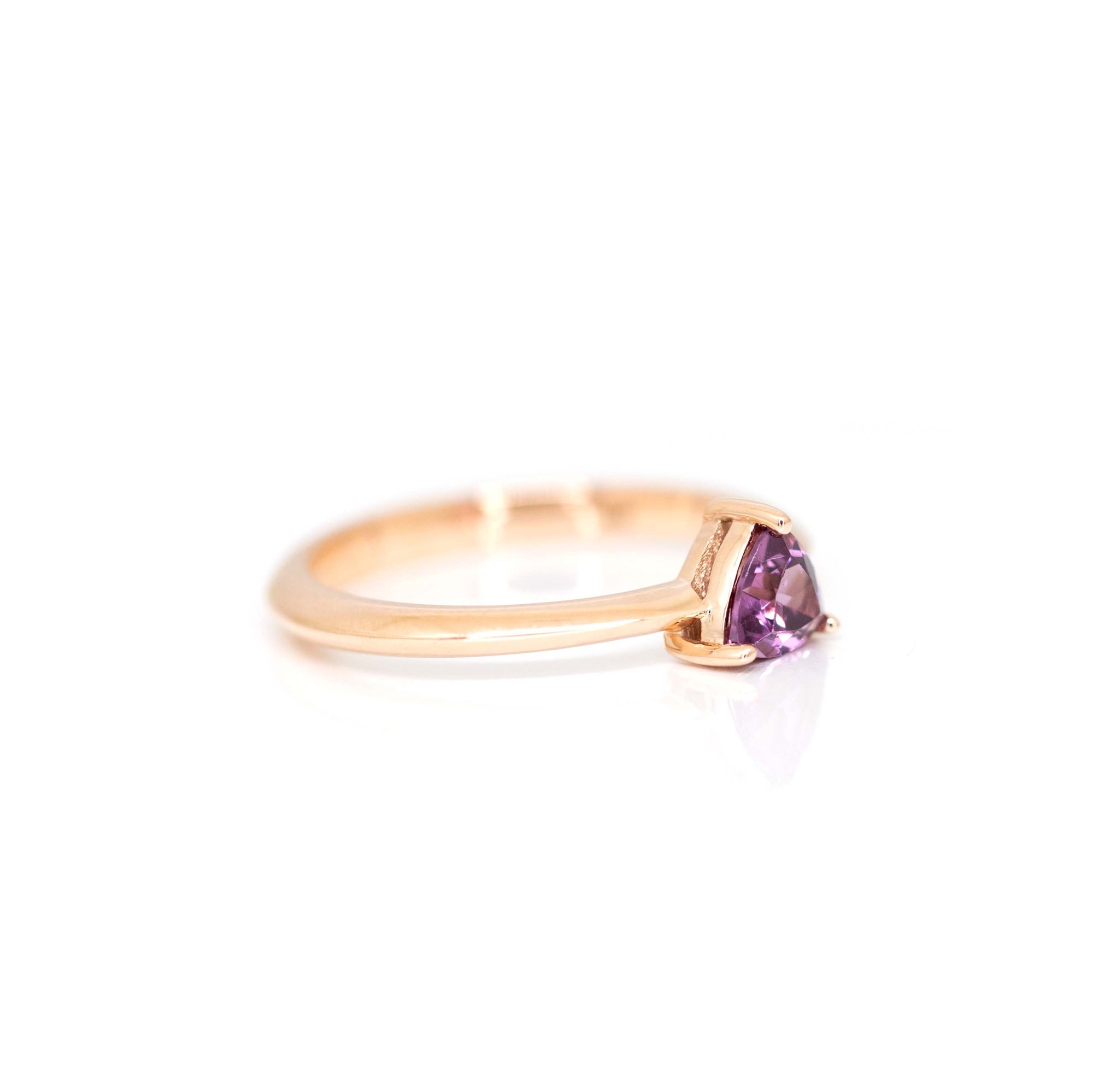 side view of rose gold ring with pink violet trillion garnet gemstone on white background